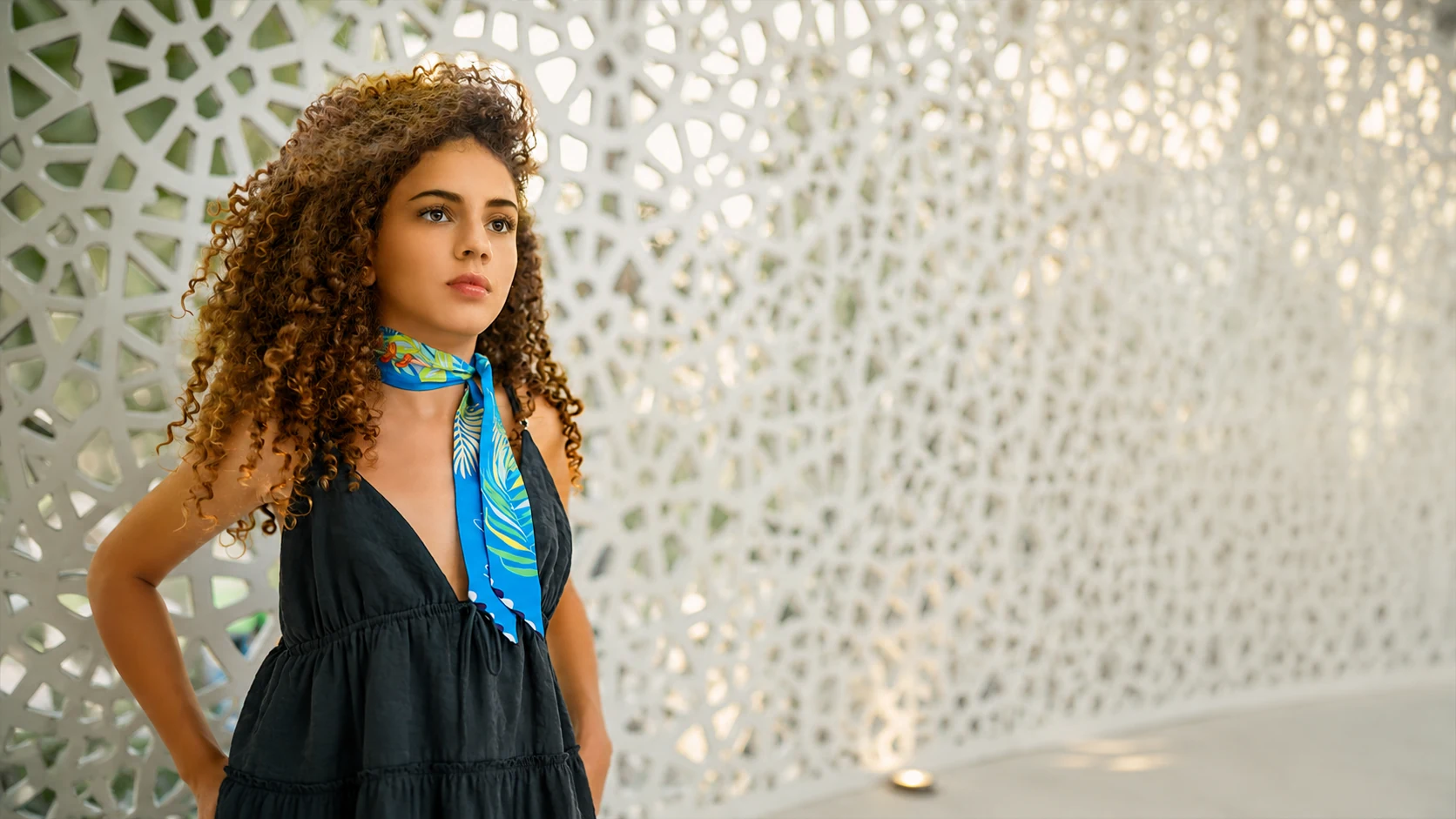 Petit twill di seta NinaMoire azzurro annodato al collo, davanti alla facciata traforata